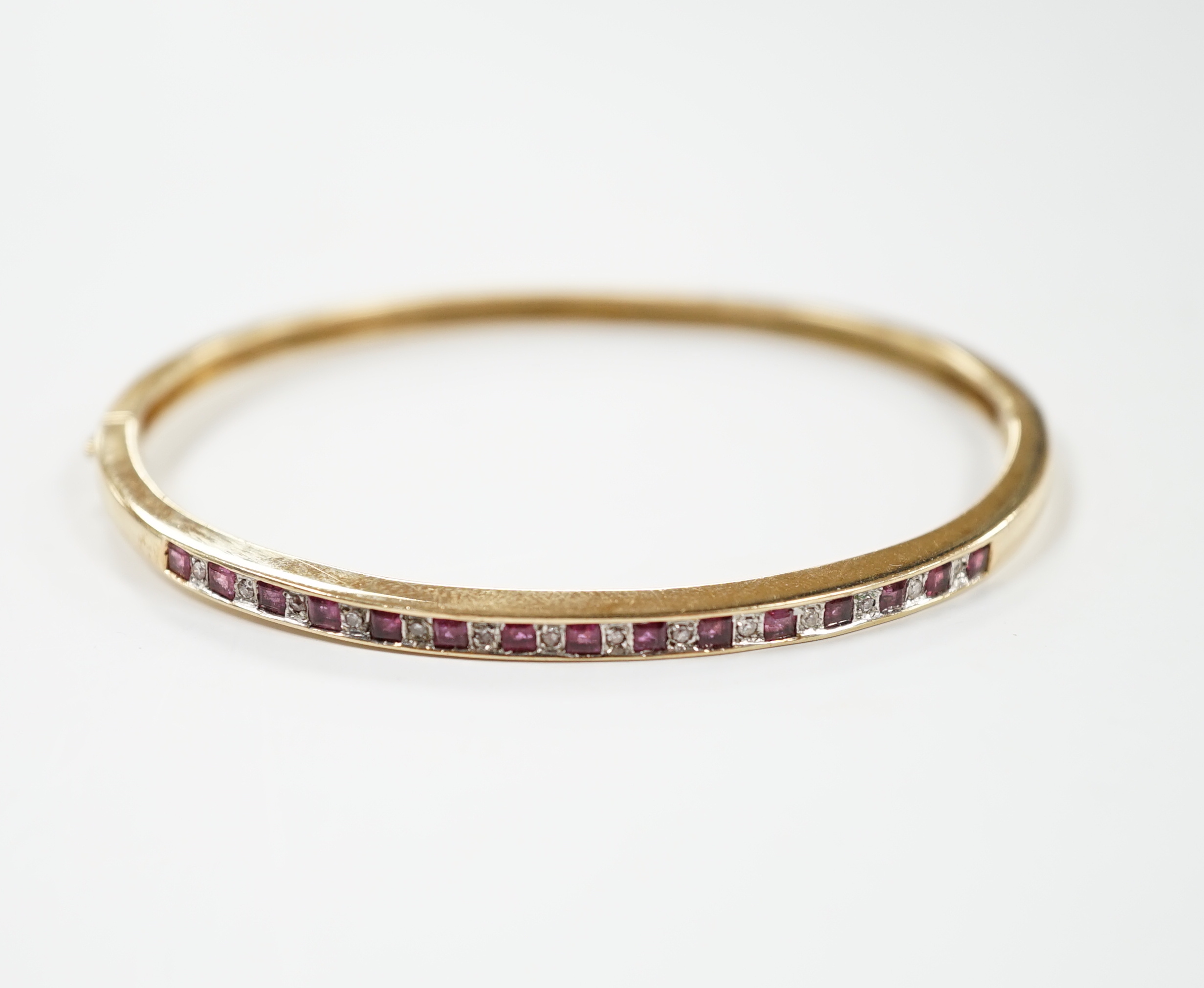 A yellow metal, ruby and diamond chip channel set hinged bangle, interior diameter 57mm, gross weight 10.8 grams.